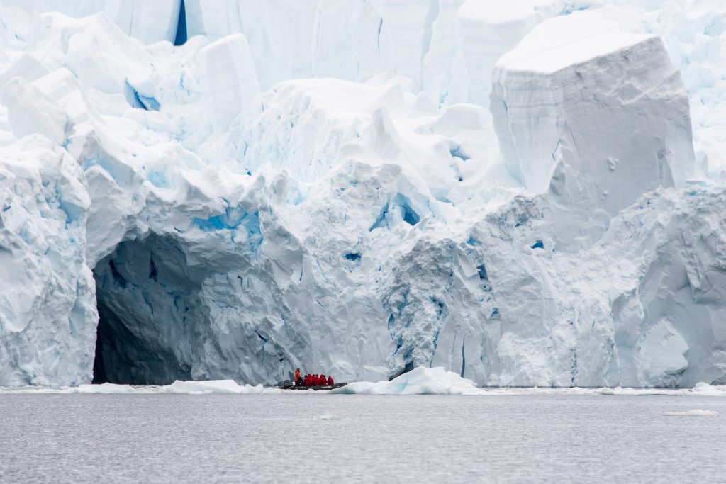 Zodiac full of guests on the water in front of huge glacier face in Antarctica. 