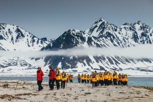 Group of guests walking on shore with mountain peaks in background.