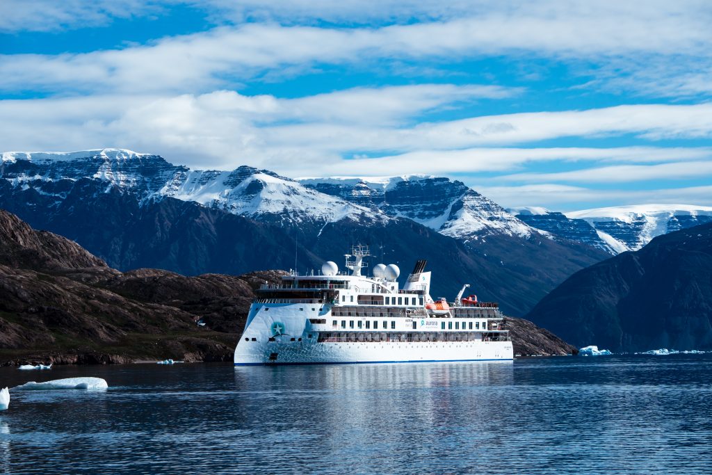 The ship Greg Mortimer on the water with mountains in background.