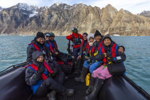 A zodiac full of guests with rugged mountains in background.