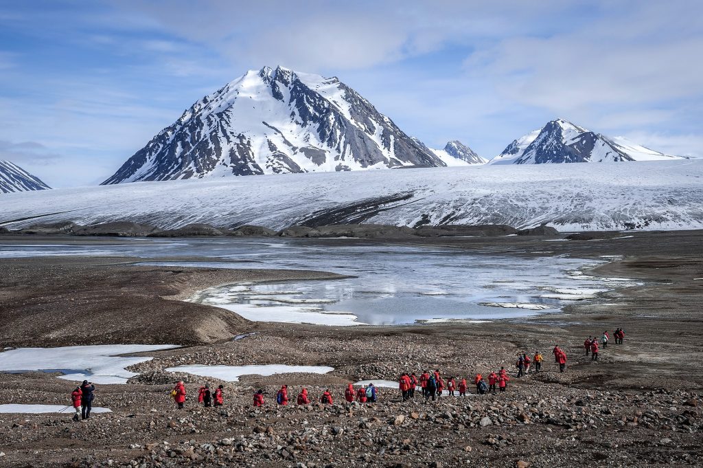 Guests hiking on shore with mountain peak in background. 