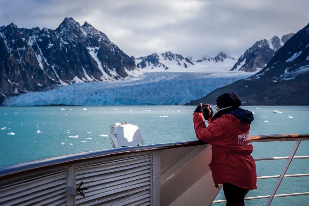 Guest on deck of ship looking at scenic glacier in Svalbard. 