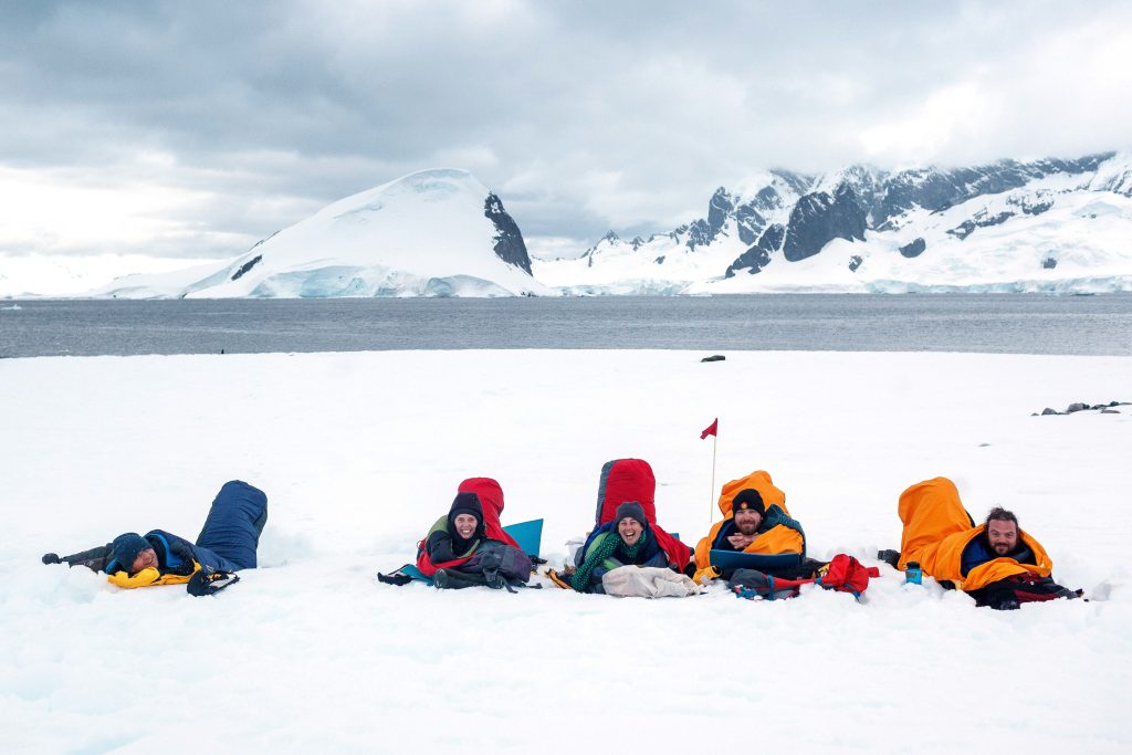 campers laying in sleeping bags on snow in Antarctica.