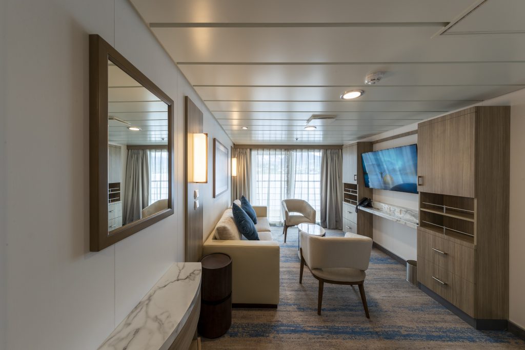 Living area with couch, 2 chairs, flat screen TV and sliding glass door.