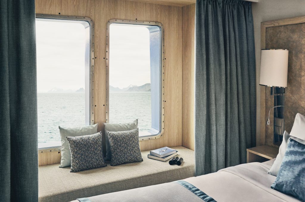 Bench sofa next to bed in front of 2 large windows.