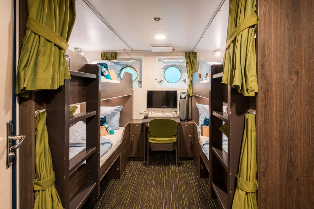 Quad cabin on Ortelius showing 2 upper and 2 lower berths plus small desk and 2 porthole windows.