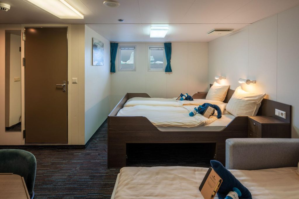 Superior cabin on the Ortelius showing 1 double bed, 1 single bed and 2 small windows.