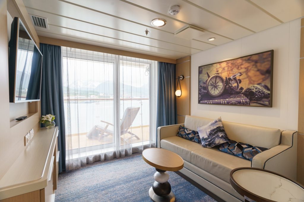 Sitting area with white couch, small coffee table, tv and floor to ceiling window leading to private balcony