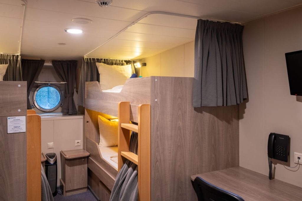 bunk beds, porthole window and small desk inside Quad cabin on Plancius