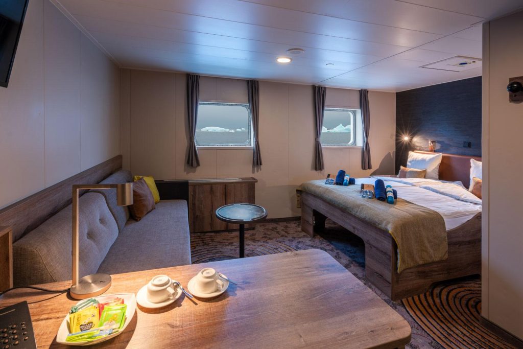 Interior of a Superior cabin on the ship Plancius with a desk, double bed, couch and 2 windows.