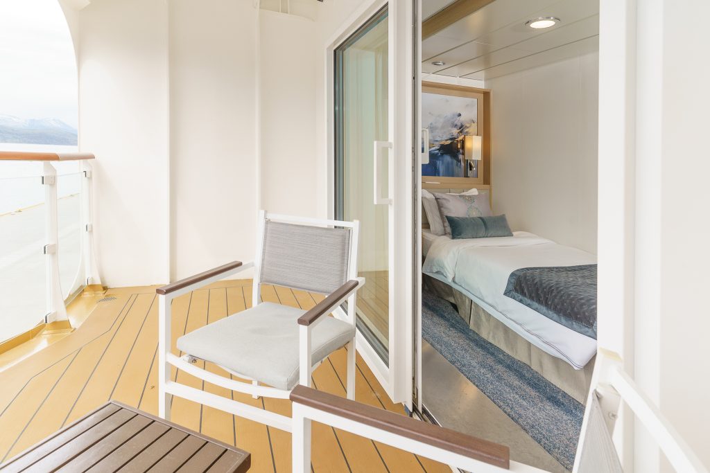 Balcony with 2 chairs, small table and sliding door open with view of twin bed.