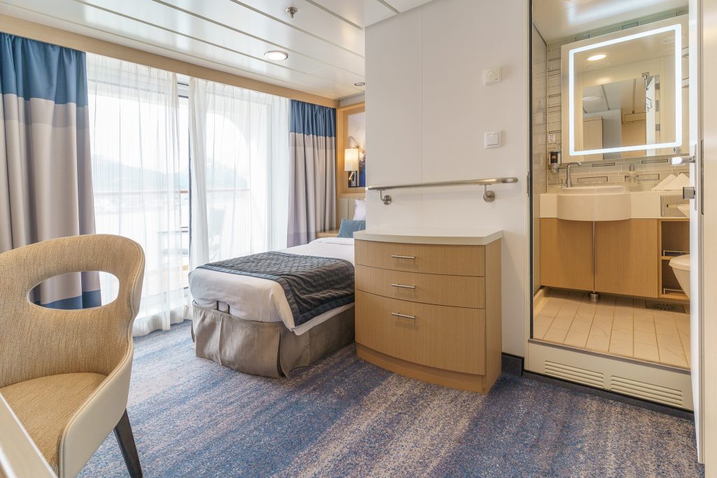 Studio Single Veranda on Ocean Explorer with 1 twin, chair, glass sliding door and door open to bathroom.