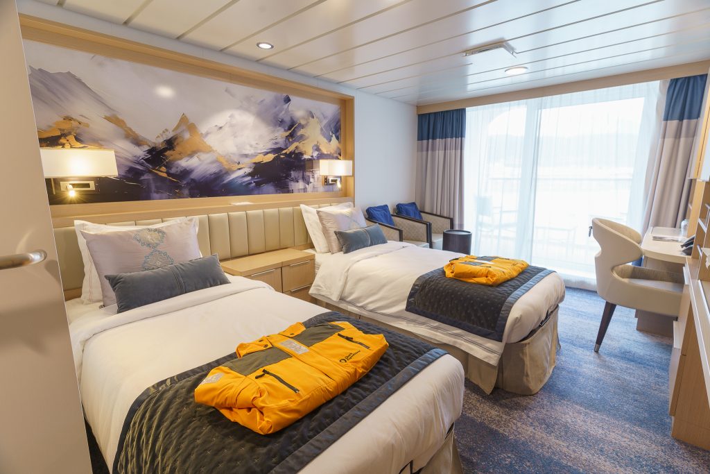 Interior of Veranda Stateroom on Ocean Explorer with 2 twin beds, chair and large windows.