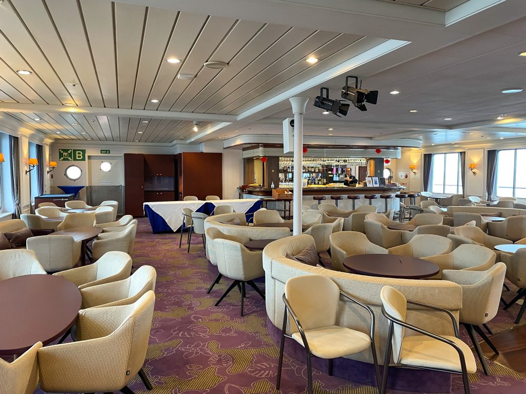 Club lounge on the ship Seaventure showing multiple empty tables & chairs plus a bar.