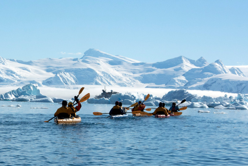 kayakers paddling in Antarctica with a ship and mountains in background