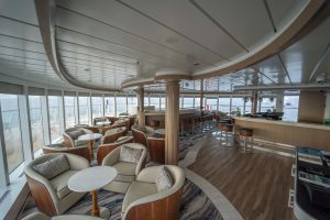 Greg Mortimer observation deck lounge with individual chairs, barstools, small tables, bar area and huge windows.