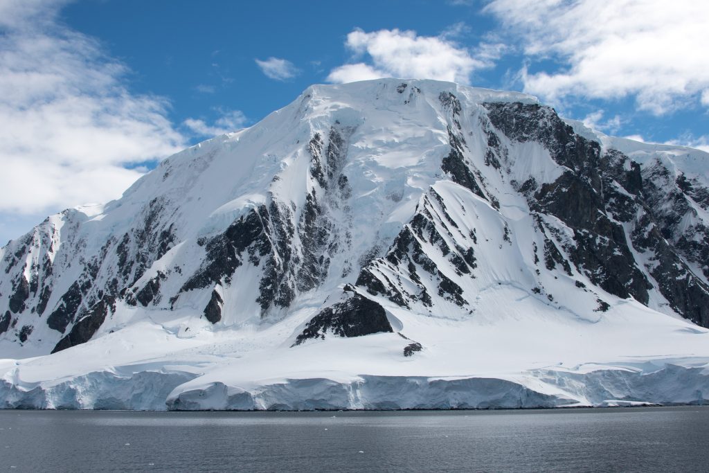 Rugged snow covered mountain rising out of water.