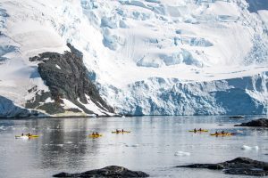 Kayakers paddling next to large glacier face. 