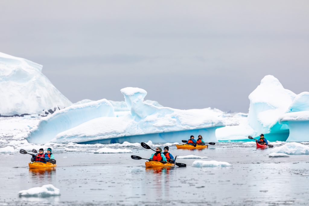 Guest kayaking in Antarctica with icebergs in the background