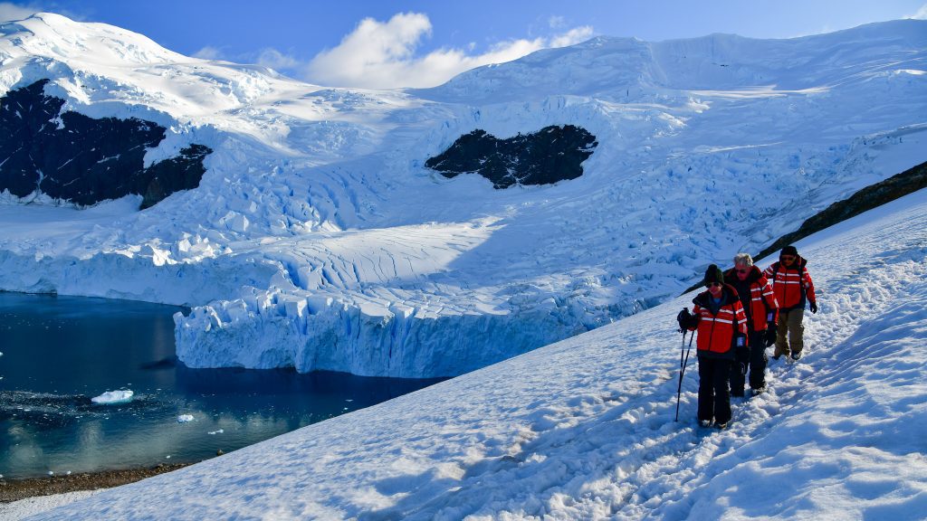 Guests hiking in snow next to glacier.