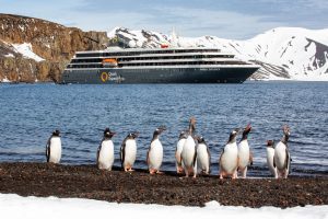 The ship World Explorer on the water with penguins on the beach.