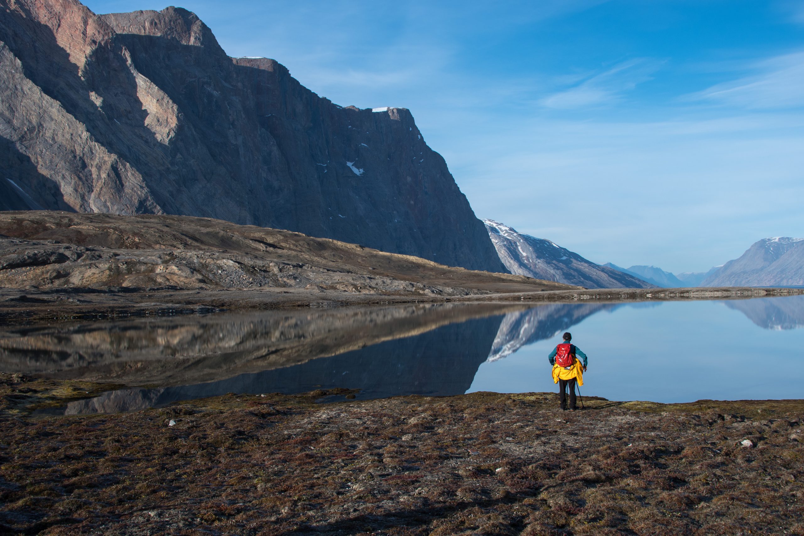 A guest gazing at lake and large fjord with steep cliffs in East Greenland.