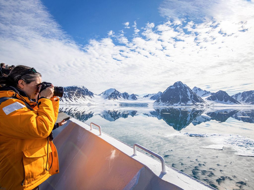 Guest standing on deck of ship taking photos of Arctic landscape.