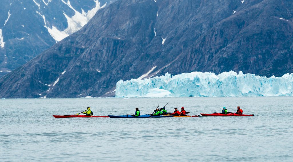 Kayakers on the water with icebergs in background.