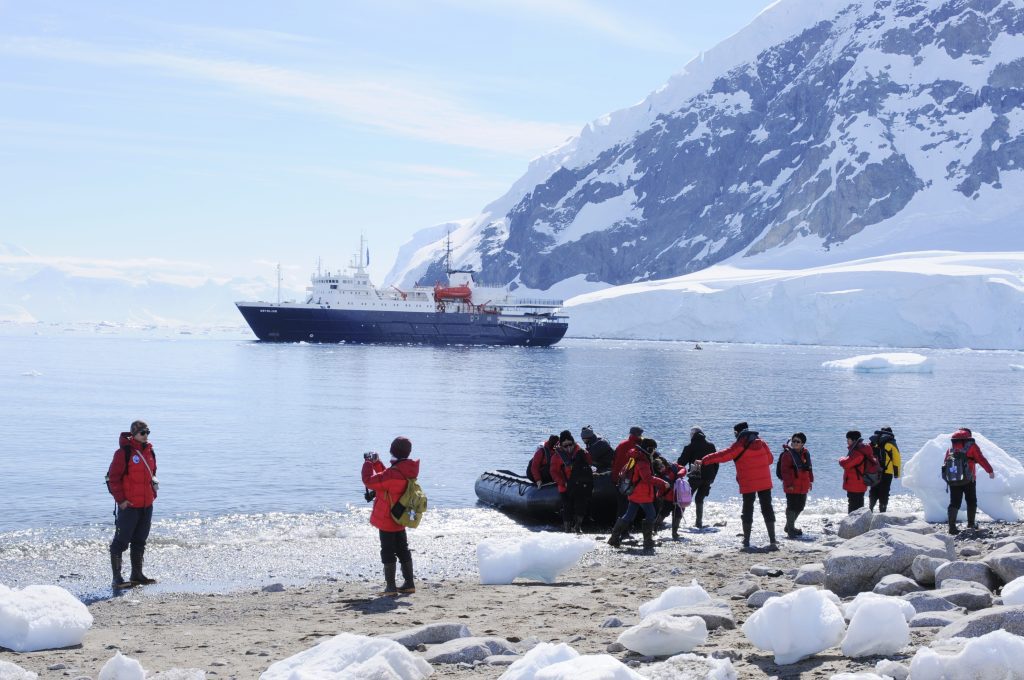 Guests standing on shore in Antarctica with ship in the background.