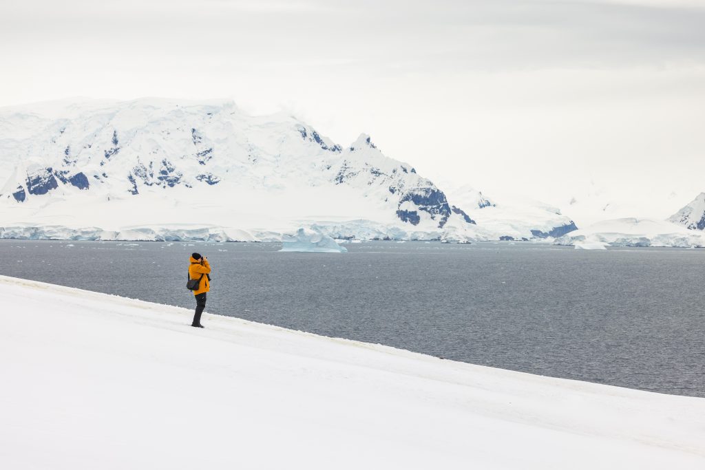 Solo guest standing on snowy hillside overlooking ocean.