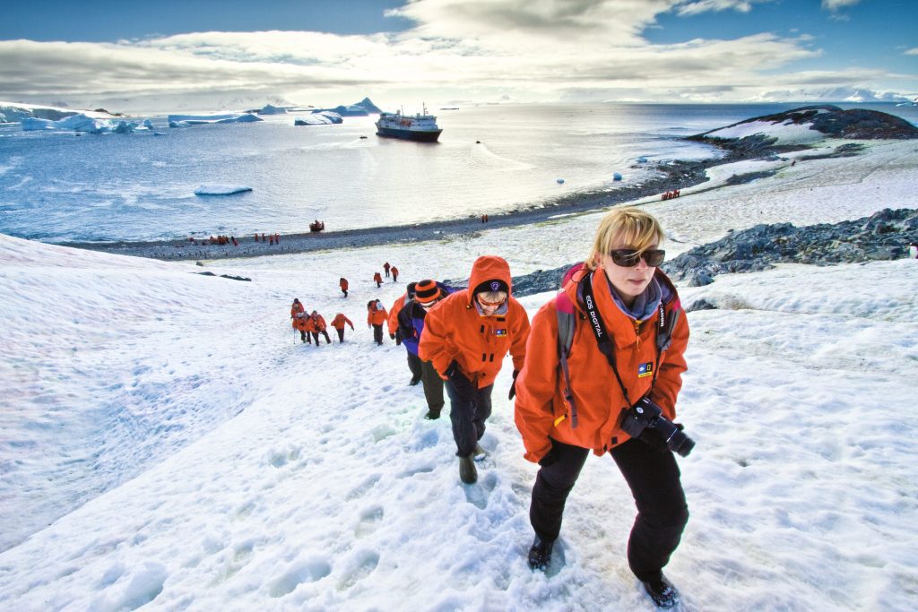 Guests walking up snowy hillside with ship in background.