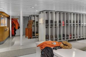 Rows of lockers with large boots stored inside and bench with orange parka in the mudroom on the National Geographic Explorer.