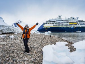 Passenger standing on beach in Antarctica with ship in background. 