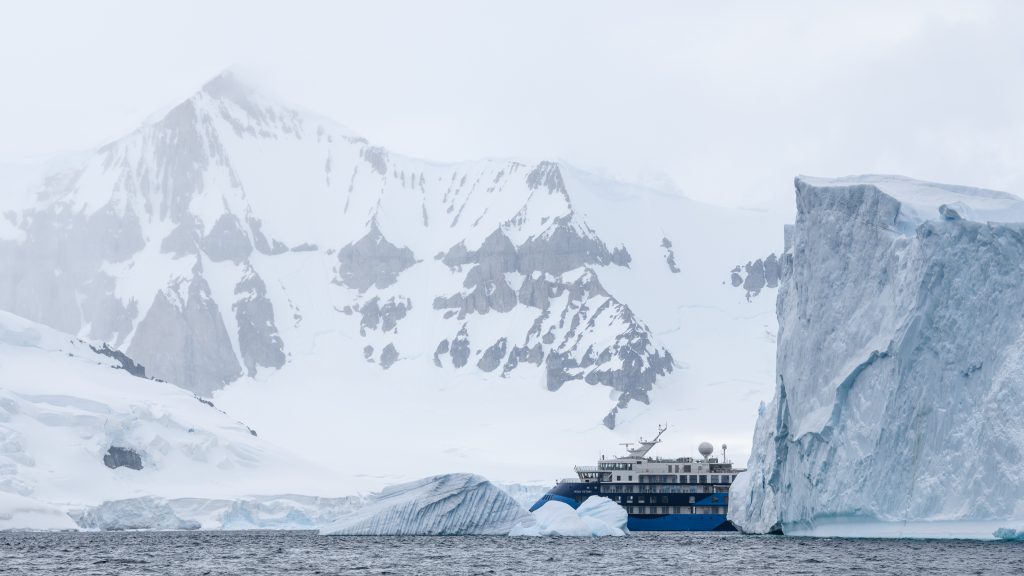 Ship sailing around gigantic iceberg in Antarctica.