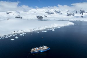 Birds eye view of ship sailing next to snowy shoreline.