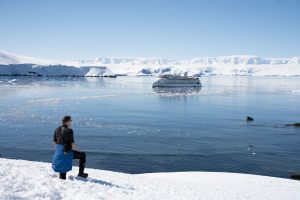 Guest standing in snow looking towards ship in the water.