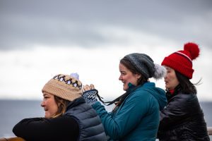 Three female guests standing on deck of ship looking at ocean. 