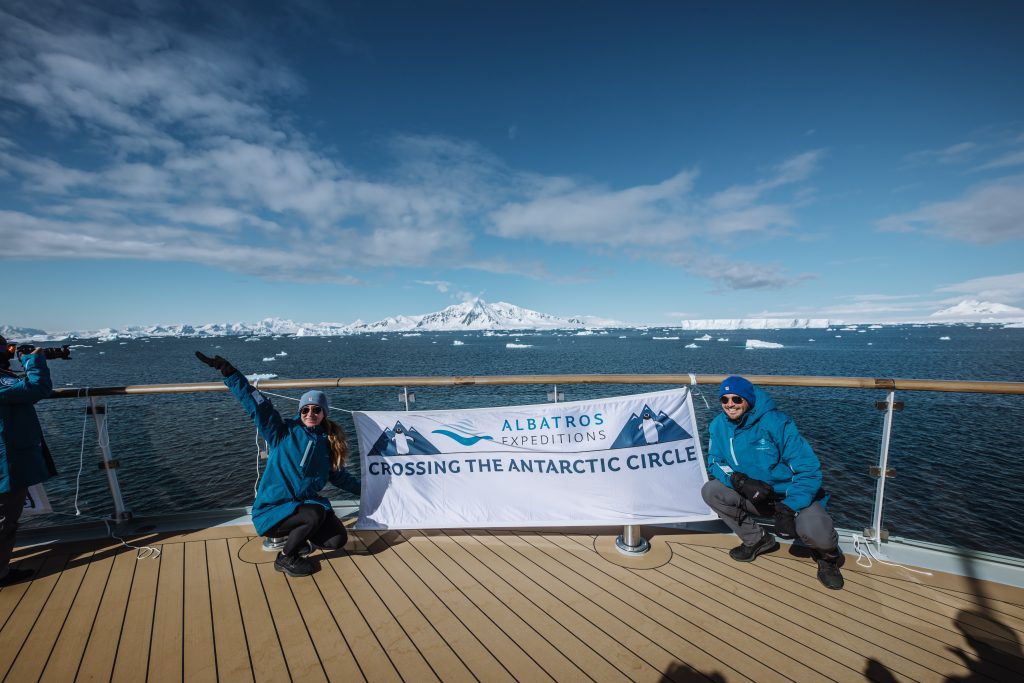 Guest holding Antarctic Circle banner on deck of ship.