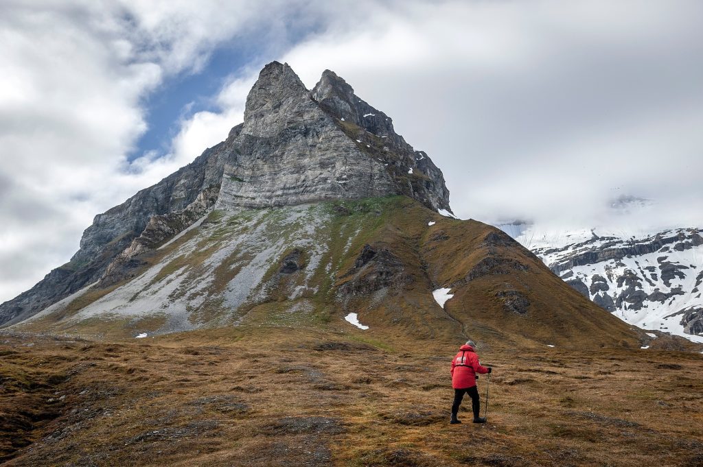 Guest hiking in front of jagged mountain peak in Svalbard. 