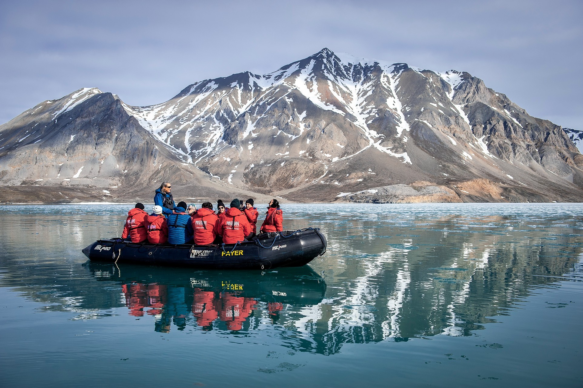 Guests in zodiac on calm water with stunning mountain scenery.