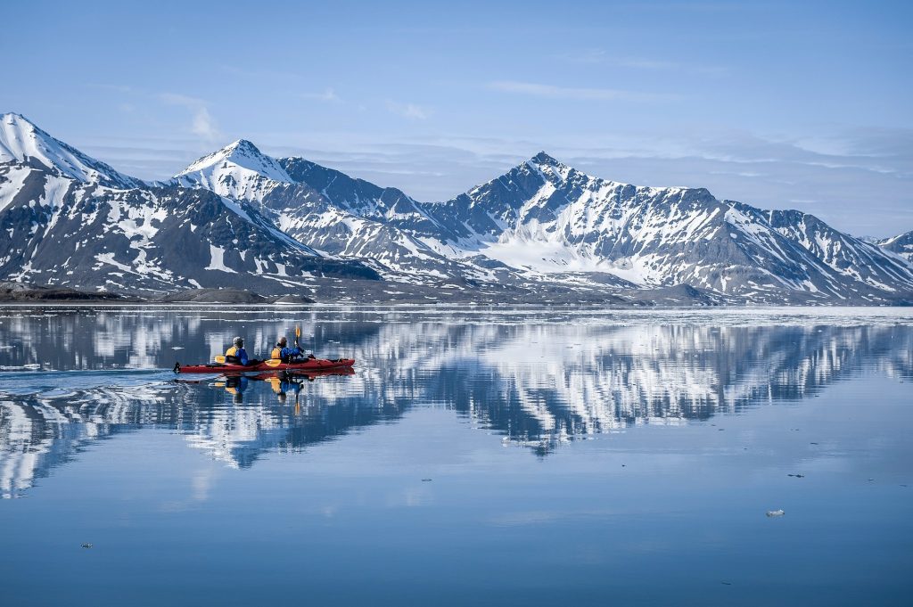 Kayakers on still water with snowy mountains in background. 