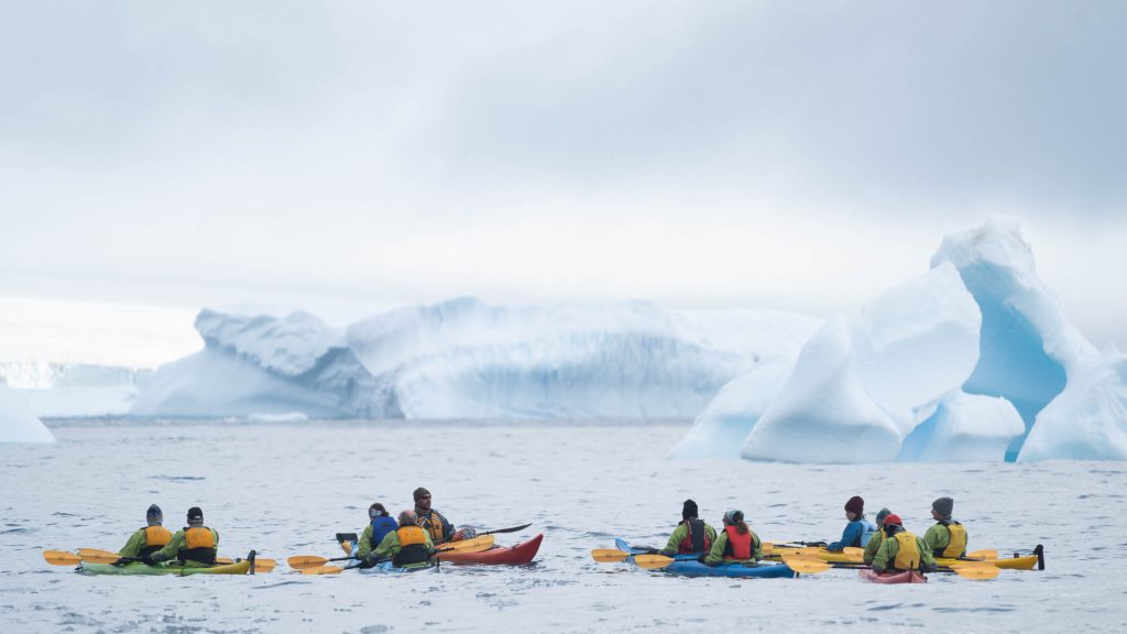 Kayakers on the water with icebergs in background.