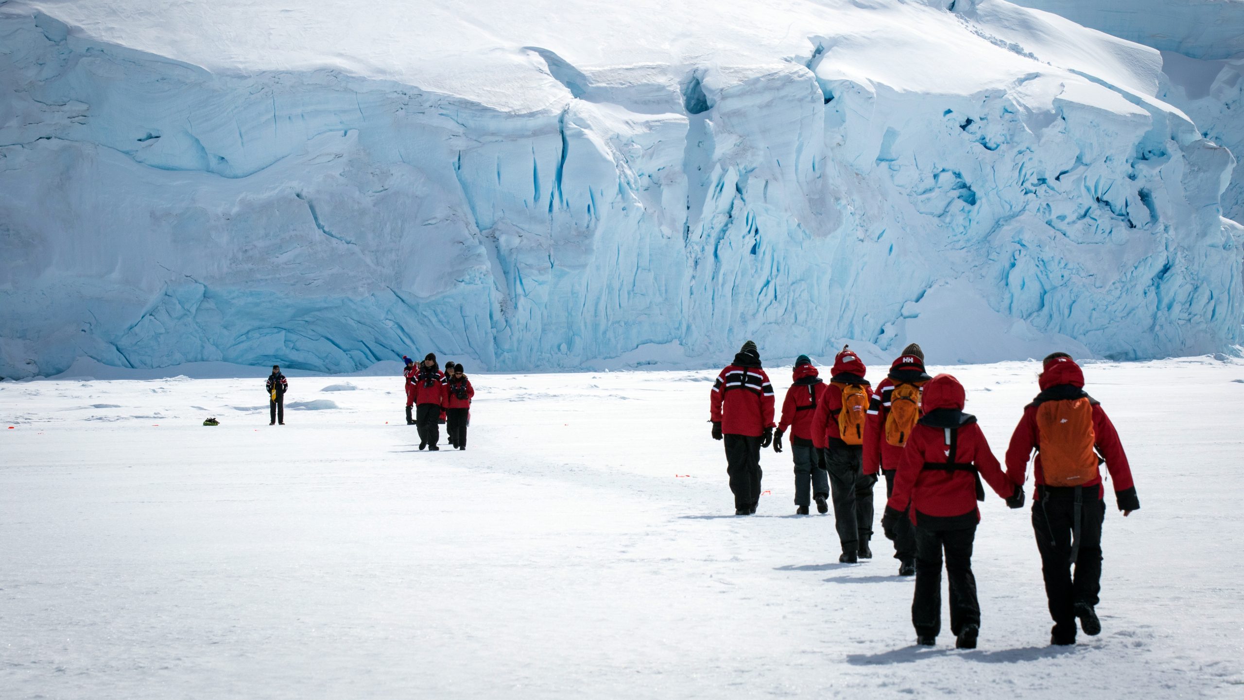 Guests walking on fast ice near glacier face.