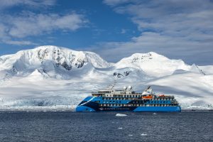 The ship Ocean Albatros on the water in front of snow covered mountains.